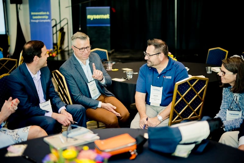 A group of members at the NYSCIO conference, gathered in a loose circle, in mid-conversation.