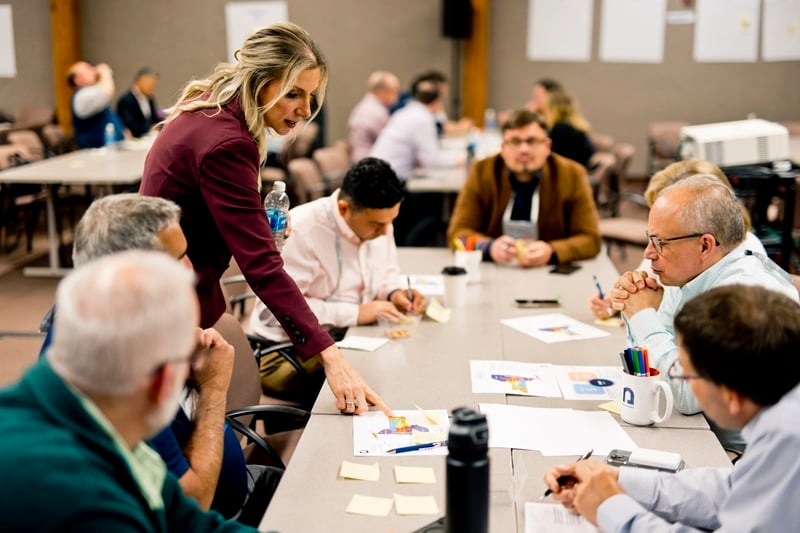 Chief Information Security Officer Emilyann Fogarty points to a paper on a table. Nysernet members lean in around the table.