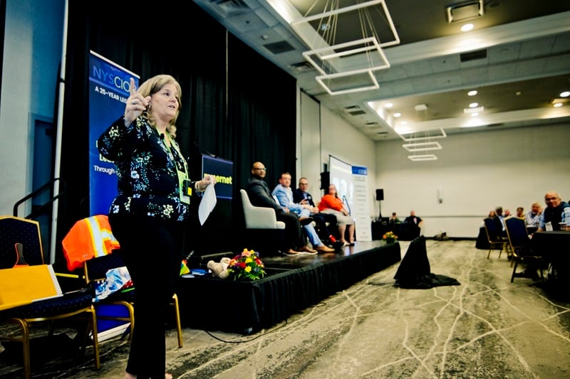 Nysernet CEO and President Jeanne Casares is in the foreground addressing the Nysernet community while a panel of Nysernet members is on stage in the background
