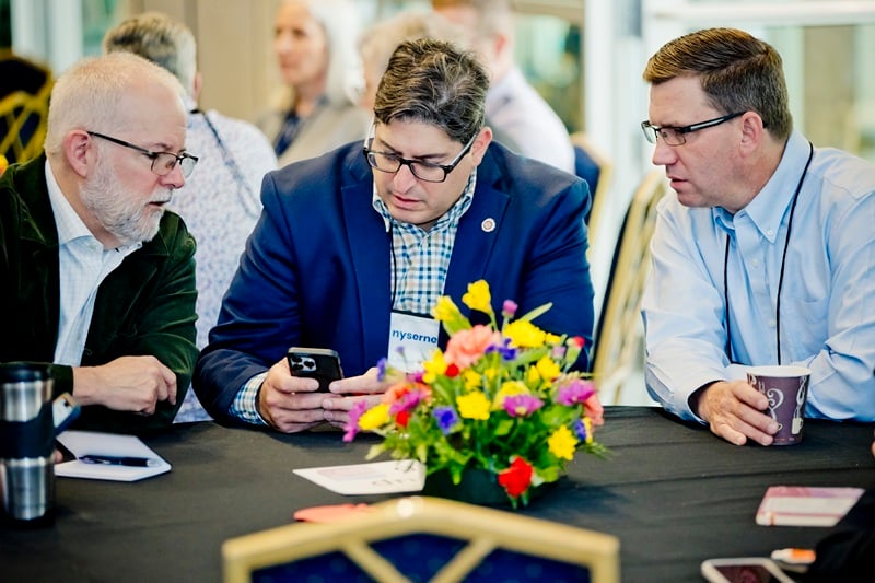 three Nysernet members seated at a table, hovering over a mobile device.