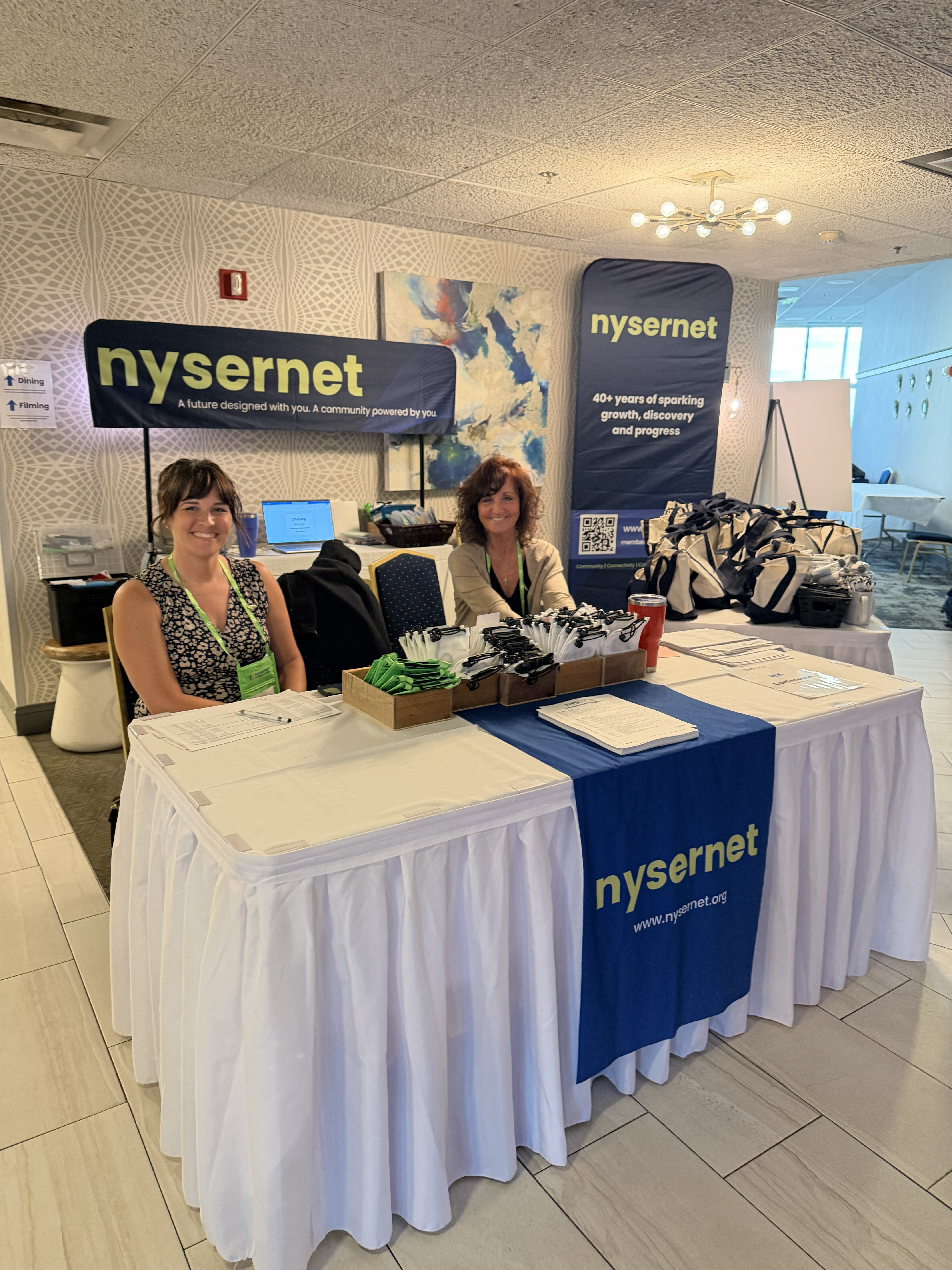 Members of the Nysernet team sit at a registration table decorated with Nysernet banners and signage.