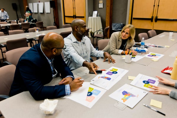 3 individuals seated at a table discussing the papers laid out in front of them.