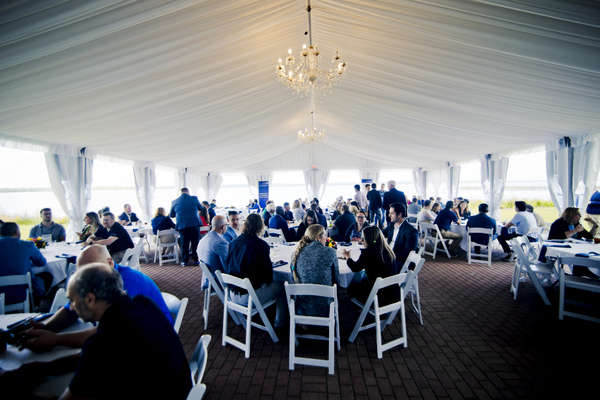Conference attendees seated at round tables underneath a tent on the shore of Seneca Lake