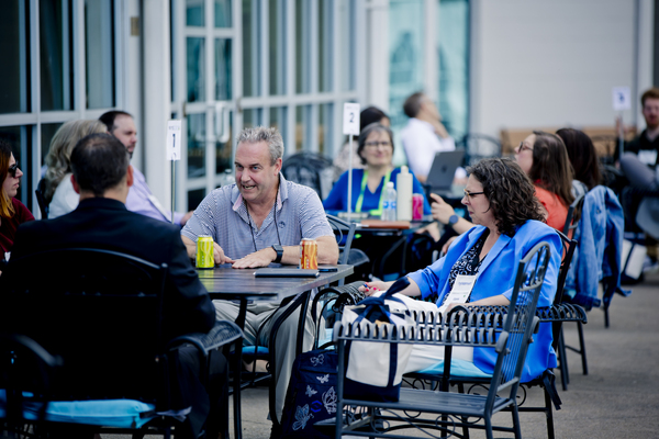 Conference attendees in conversation at tables on the patio